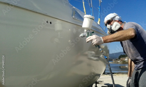 man with face mask spray painting sail boat yacht with air gun	