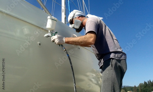 man with face mask spray painting sail boat yacht with air gun	