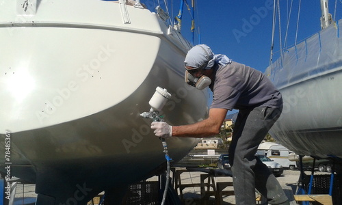 man with face mask spray painting sail boat yacht with air gun	