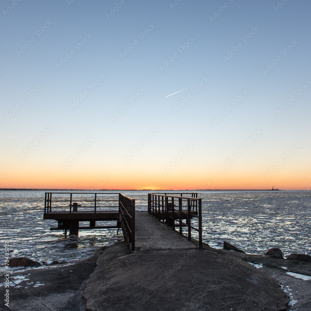 sunset over frozen sea with old metal bridge