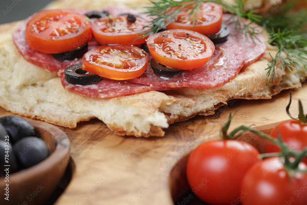 flat pita bread with salami and vegetables on wood table