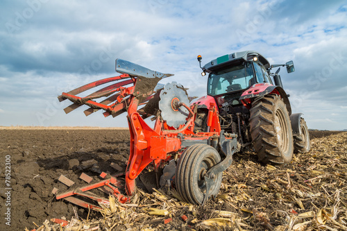фотографія Farmer plowing stubble field with red tractor