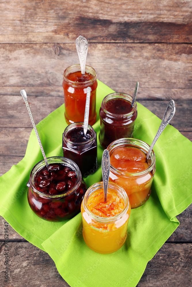 Jars of tasty jam with napkin on wooden background Jars of tasty jam with napkin on wooden background