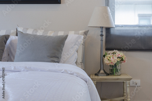 grey pillow on bed with lamp and plant on wooden table in bedroo photo