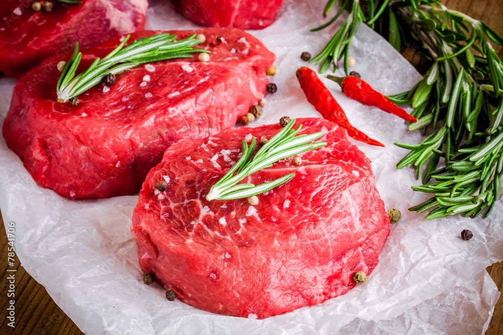 two raw steaks with rosemary, garlic, salt and pepper