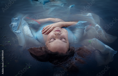 Young beautiful drowned woman in blue dress lying in the water