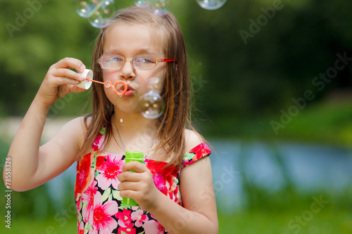 Little girl having fun blowing soap bubbles in park.
