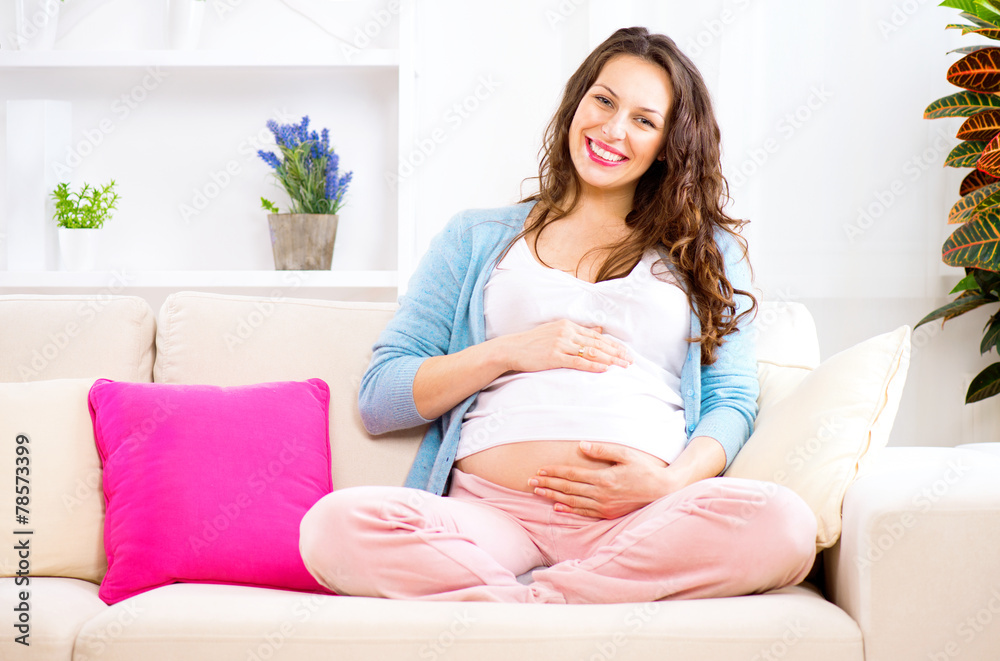 Pregnant smiling woman sitting on a sofa and caressing her belly Pregnant smiling woman sitting on a sofa and caressing her belly