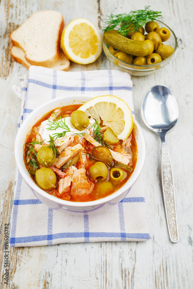 Soup saltwort with lemon, meat, pickles, tomato sauce olives in a bowl on a sacking, bread on a wooden board background