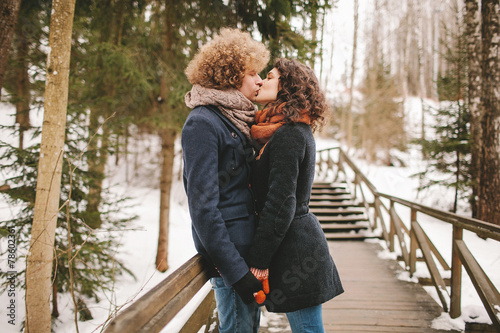 Hipster couple kissing on wooden stairs in winter park