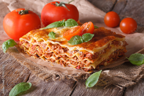 Italian lasagna with basil close-up on paper, horizontal rustic
