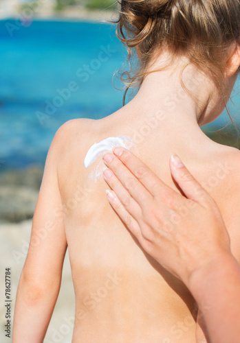 Woman s hand applying suntan cream on child back.