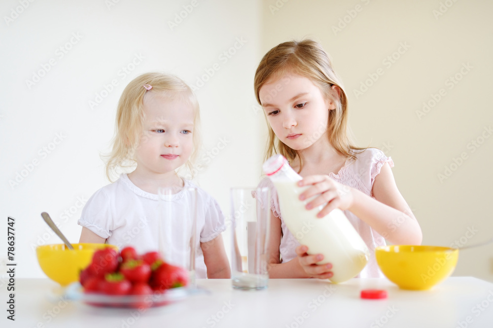 Two cute little sisters eating cereal in a kitchen Two cute little sisters eating cereal in a kitchen
