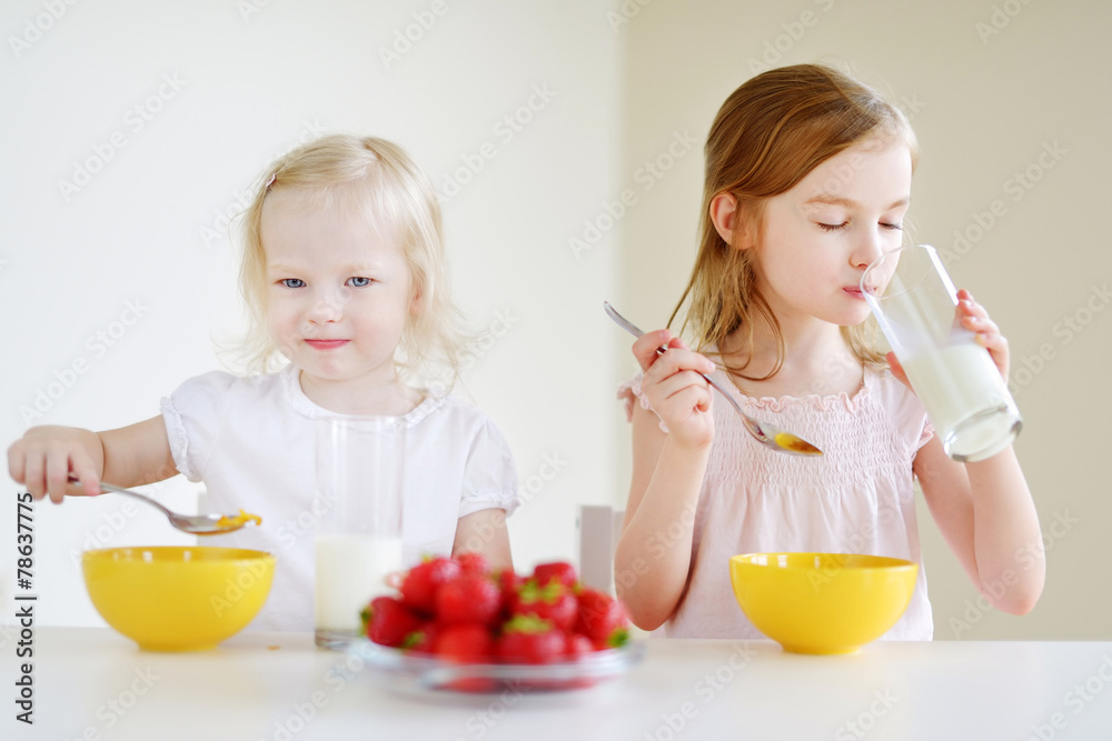 Two cute little sisters eating cereal in a kitchen Two cute little sisters eating cereal in a kitchen