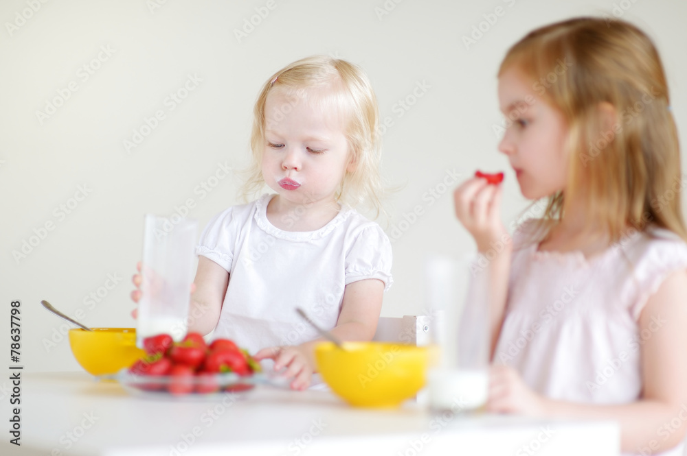 Two cute little sisters eating cereal in a kitchen Two cute little sisters eating cereal in a kitchen