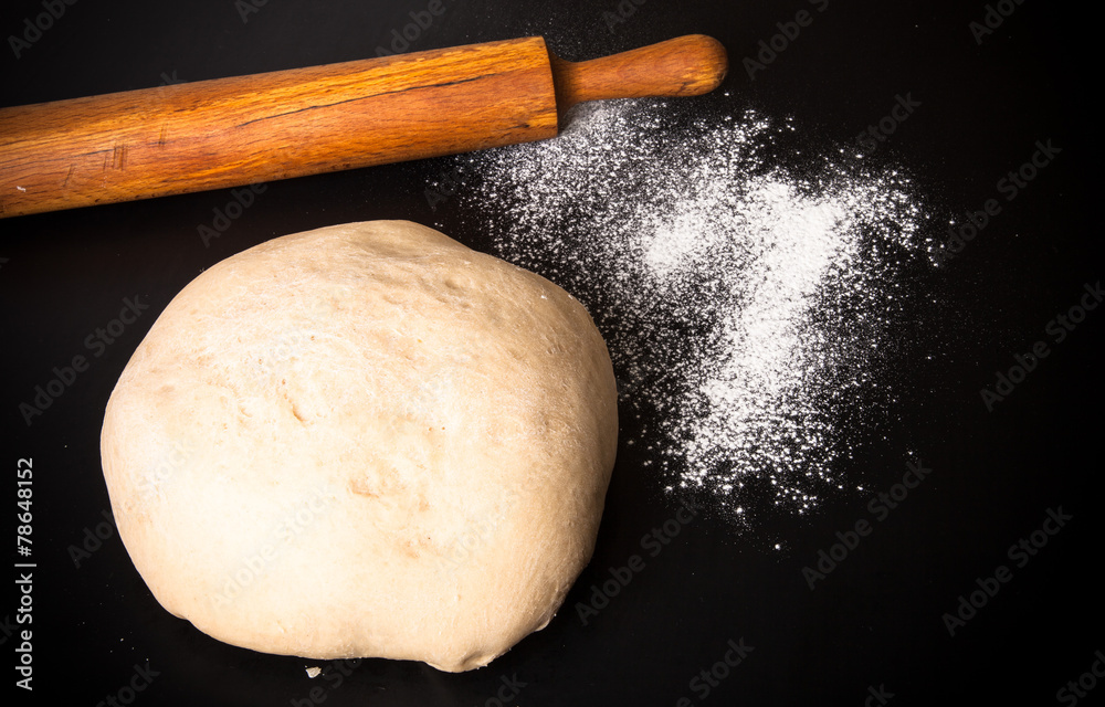 Dough, rolling pin and flour on a black background Dough, rolling pin and flour on a black background