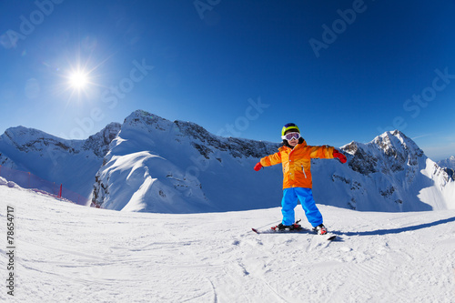 Happy boy in ski mask with arms apart skiing alone