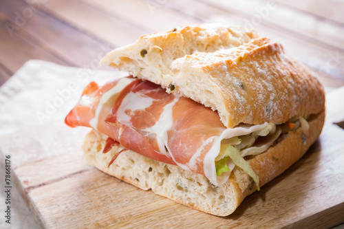 Sandwich with parma ham and salad on wooden cutting board