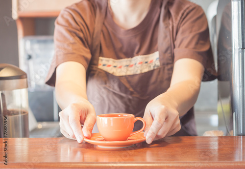 Barista offering mini orange cup of coffee