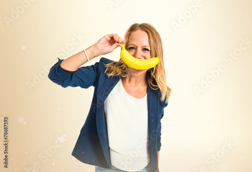 Blonde girl with banana as moustache over white background