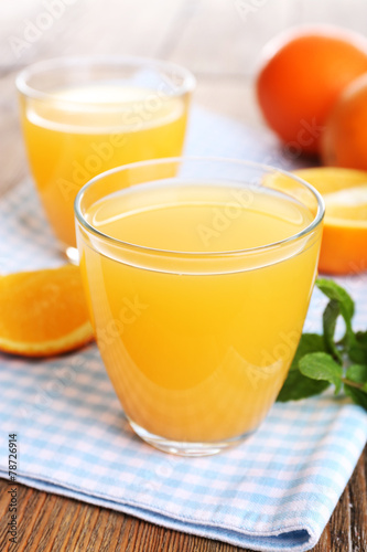 Glasses of orange juice with oranges on wooden table close up