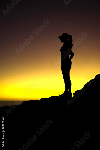 Silhouette of runner wearing hat at the top of oceanside trail
