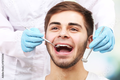 Examine of young man by dentist on light blurred background