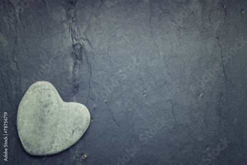 Gray zen heart shaped rock in the corner on a tile background