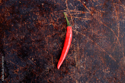 Single red thai chili pepper on brown rustic background