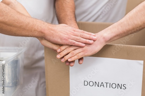 Volunteer team holding hands on a box of donations
