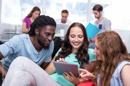 Students using digital tablet with friends in background