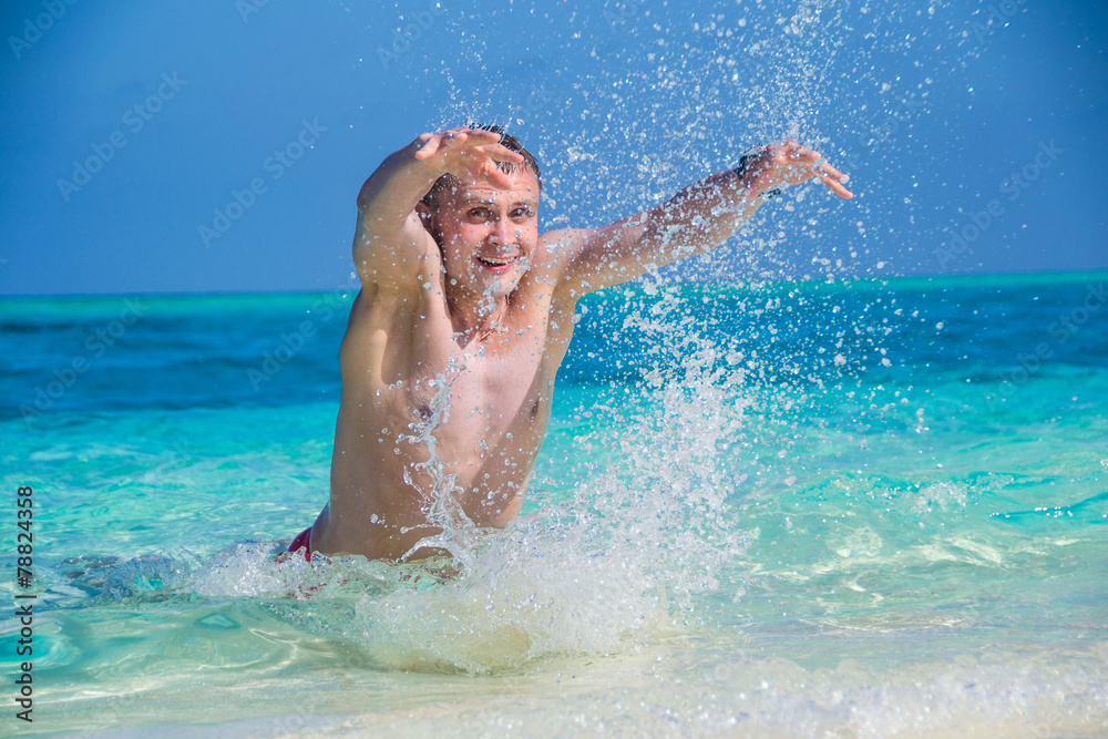 happy man makes a splash of water on tropical beach, close up