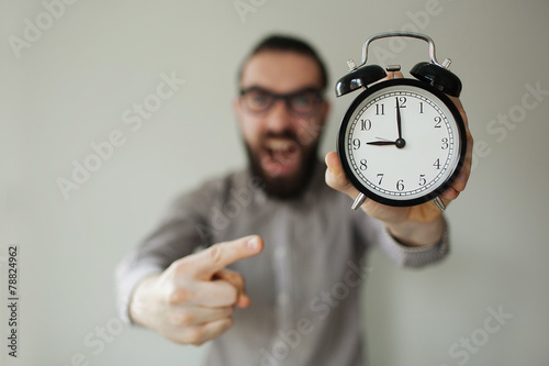 Angry boss with beard holds alarm clock screaming on camera