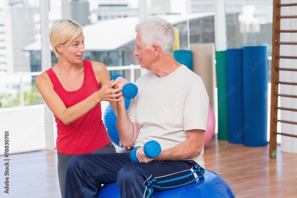 Fototapeta premium Female trainer assisting senior man in lifting dumbbells
