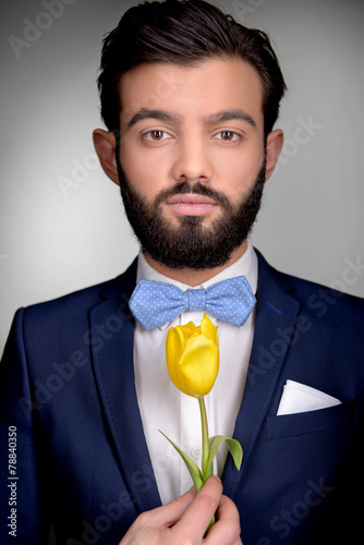 Stylish man with beard and bow tie holding tulip