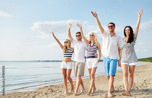 smiling friends walking on beach and waving hands