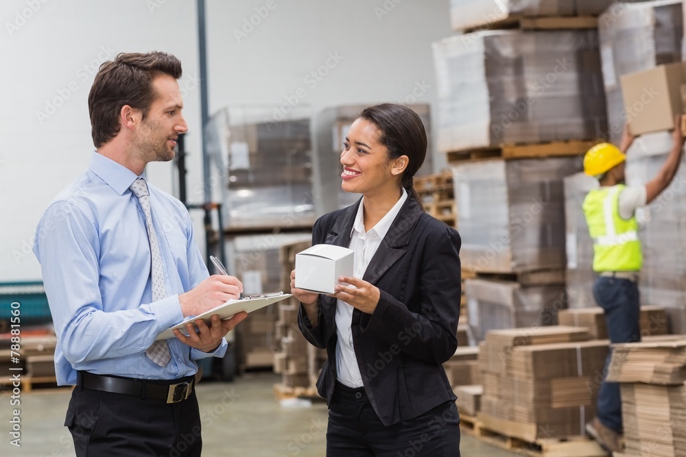 Smiling warehouse managers holding box and clipboard Smiling warehouse managers holding box and clipboard