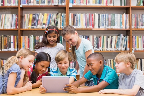 Cute pupils using tablet computer in library