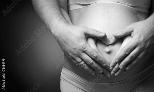 Pregnant belly with hands of mother and father making heart