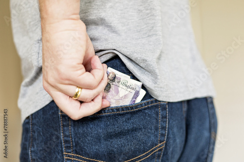 Man puts cash bank notes into back pocket of jeans