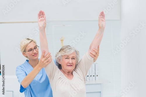 Female nurse helping female patient in exercising
