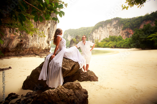 Tableau sur toile groom looks at bride sitting on rock at sand beach