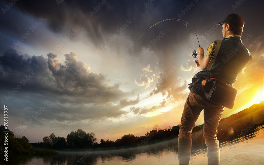 Young man fishing at dramatic sunset - obrazy, fototapety, plakaty 
