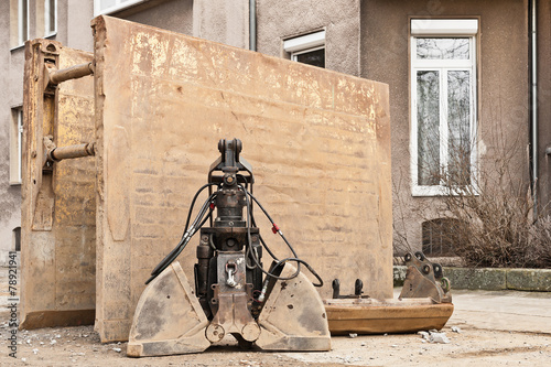 Eine Bagger-Doppelschaufel steht vor einer grossen Verbauplatte photo