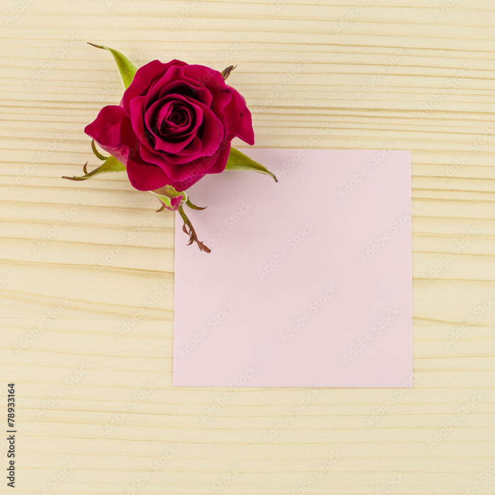 Blank pink paper and rose flower on wooden background