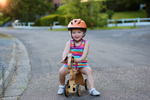Toddler girl driving wooden tricycle on the street