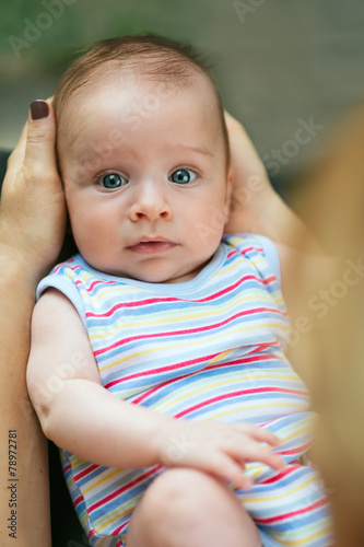 Adorable baby held in his mother’s lap looking at camera