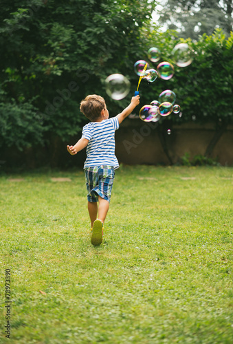 Cute 5 year old boy running making soap bubbles