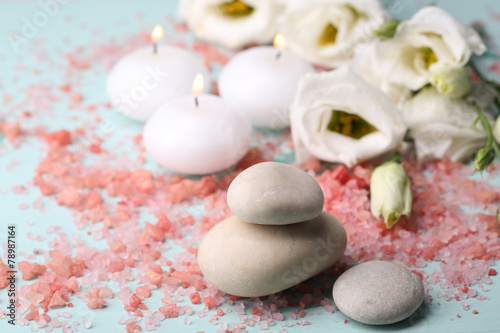 Spa stones with candles and flowers on blue background close-up