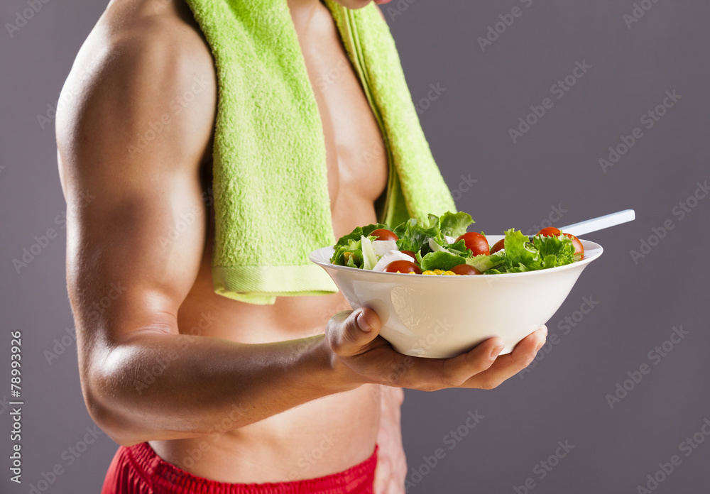 Fit man holding a bowl of fresh salad on grey background